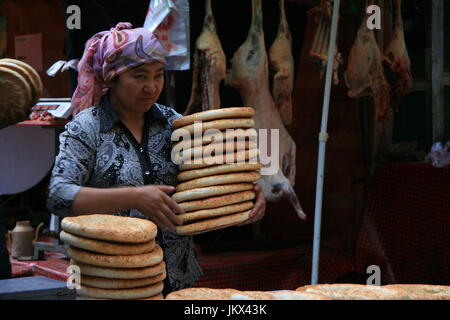 La donna che porta una pila di pane pita in vendita nella città vecchia Urumqi Foto Stock