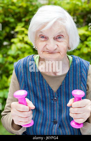 Foto di eccitato donna anziana facendo sport esercizi all'aperto nel giardino, azienda rosa manubri Foto Stock