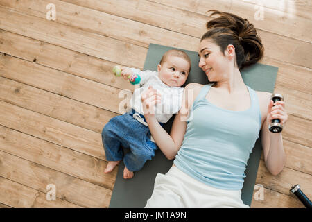 Vista superiore della madre con bambino sdraiato sul pavimento e giocando con manubri Foto Stock