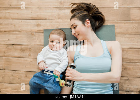 Vista superiore della madre con bambino sdraiato sul pavimento e giocando con manubri Foto Stock