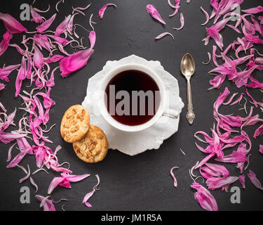 Nero caffè in tazza con due biscotti e peonia petali sparsi intorno Foto Stock