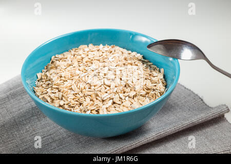 Fiocchi di avena in ceramica blu ciotola pronto per cucinare e il cucchiaio sul tavolo bianco con tessuto grigio Foto Stock