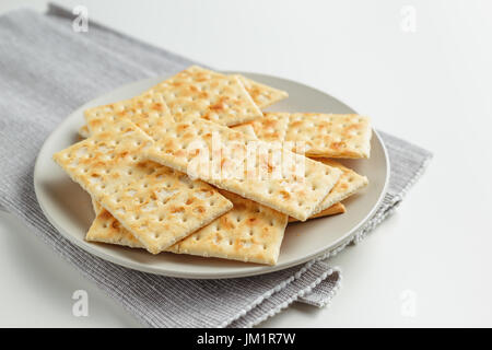 Primo piano di una piastra di uno snack. Pila di cracker sulla piastra di colore grigio e grigio igienico su sfondo bianco Foto Stock