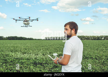 Giovane uomo operante di flying drone octocopter in corrispondenza del campo verde. Foto Stock