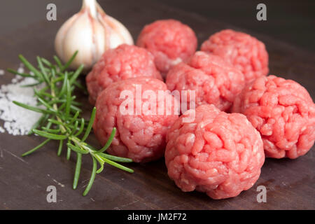 Materie le polpette di carne con aglio e rosemay su uno sfondo di legno. Preparazione di hamburger ingredienti. Foto Stock