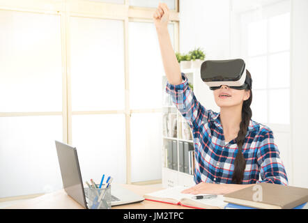 Studente utilizzando computer collegare l'e-learning con VR-dispositivo auricolare per guardare video e sollevare una mano domande quando in classe on line con insegnante in Foto Stock