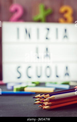 Primo piano di una serie di matite di diversi colori e una lightbox in background con il testo inizia la scuola e il ritorno a scuola in italiano, surround Foto Stock