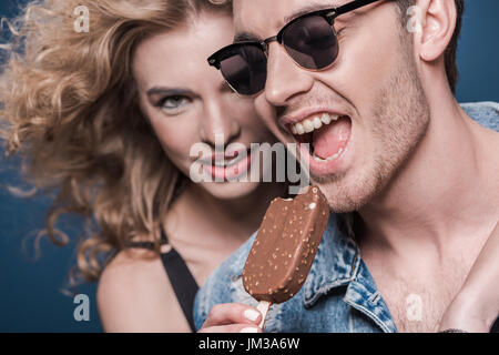 Ritratto di uomo a mangiare il gelato con la donna vicino da isolato su blu Foto Stock