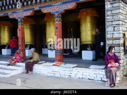 Giovane donna con il cellulare e anziane tradizionalmente condita sitiing presso il Memorial Chorten, Timphu, Bhutan Foto Stock