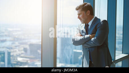 Bella coppia business executive con attraente design di stoppie, in piedi con le braccia incrociate e poggiante contro una grande finestra in un piano superiore Foto Stock