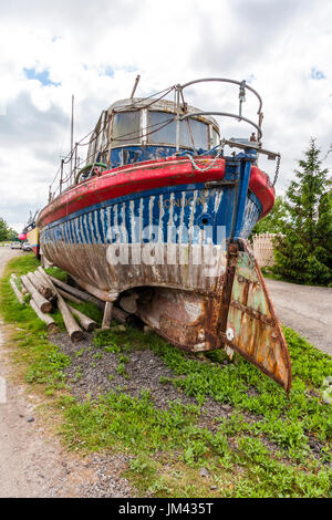 Stern vista ancorata a secco ex scialuppa di salvataggio in terra in base dock yard. Arrugginiti e blu e vernice rossa molto alterati. Ampio angolo di visione. Foto Stock