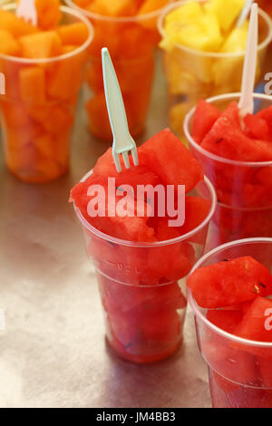 Cucina di strada, selezione di insalate di frutta, fette tagliate fresche e mature e di cocomero melone cubetti in bicchieri di plastica con forche al mercato retail display di stallo, Foto Stock