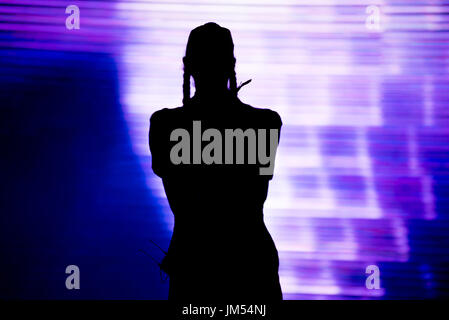 Silhouette di un artista cantare dal vivo sul palco nella parte anteriore di uno sfondo colorato Foto Stock