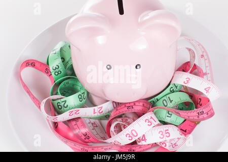 Piccola rosa in ceramica salvadanaio in aggrovigliato misurando nastri di diversi colori in piastra bianca visto dal di sopra, ritagliato close-up. Che simboleggia la salute di Foto Stock