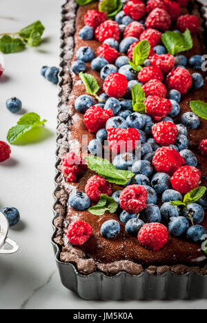 Estate in casa di pasta cotta al forno. Torta al cioccolato torta con crema di cioccolato, crudo fresco mirtillo bacche di lampone, decorato con foglie di menta, polvere di su Foto Stock