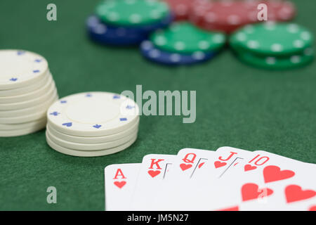 Concetto di gioco in un casinò su una serie vincente giocando a poker con una mano che mostra un royal straight flush sul verde baize con messa a fuoco per una pila di c Foto Stock