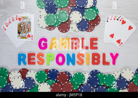 Responsabilità sul gioco d'azzardo - Vincere e perdere di mani di poker Carte visualizzate con chip casino a fianco vivacemente colorato del testo in una immagine concettuale visualizzati Foto Stock