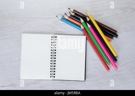 La creatività, l'arte o primario concetto di apprendimento con un fascio di matita colorata matite colorate si trovano a fianco di una doppia pagina aprire il notebook con copia spazio in un Foto Stock