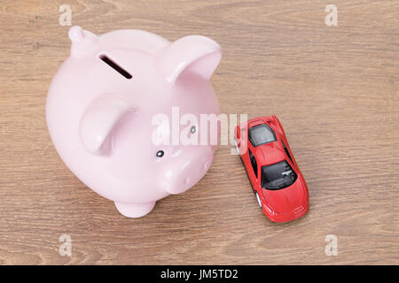 Rosa salvadanaio con red giocattolo auto in un concetto di proprietà, acquisto, i costi di esercizio del veicolo e la manutenzione è vista dal di sopra su legno Foto Stock