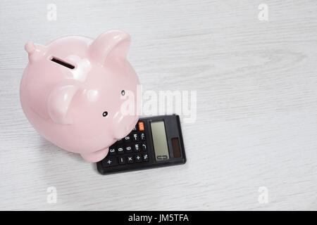 Piccola rosa lucida salvadanaio da sopra con zero su nero calcolatrice, come un concetto di raccogliere denaro con spazio di copia Foto Stock