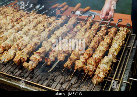 Grigliata di shish kebab su spiedino di metallo. Le mani dello chef cucinare carne arrosto barbecue con un sacco di fumo. Barbecue di carne bovina fresca tritate Fette. Tradizionale piatto orientale Foto Stock