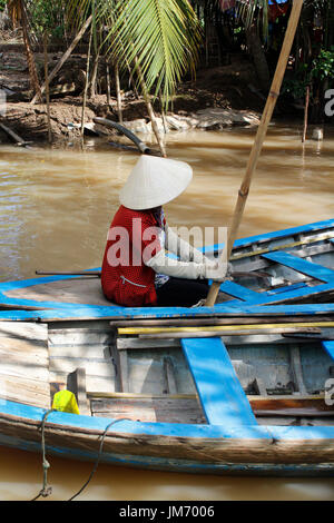 Donna vietnamita canottaggio un sampan (imbarcazione in legno) nel fiume Mekong, Ho Chi Minh Foto Stock