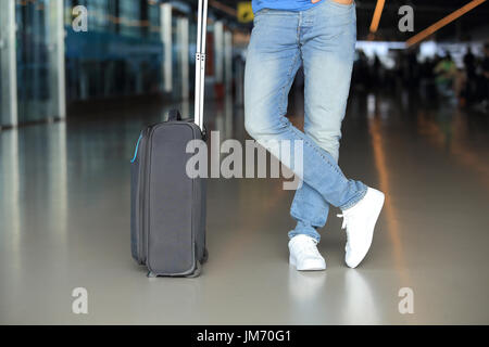 L'uomo le gambe in jeans blu e grigio valigia di close-up. Uomo con il bagaglio a mano in aeroporto. Foto Stock