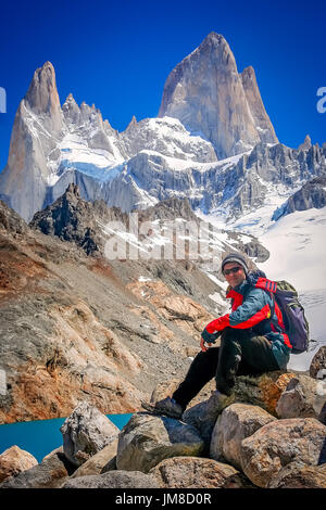 Trekker maschio poggiante sulla roccia di fronte la splendida e imponente Monte Fitz Roy vicino a El Chalten in Patagonia, Argentina Foto Stock