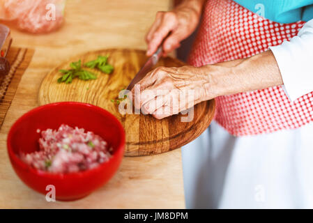 Senior donna mani tritare verdure su una tavola di legno in cucina. Foto Stock