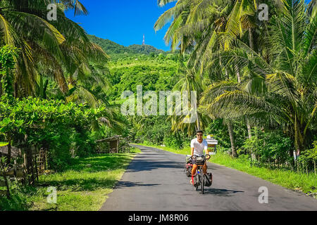 Ciclista maschio in bicicletta attraverso la fitta giungla paesaggio di Sumbava isola, Indonesia Foto Stock