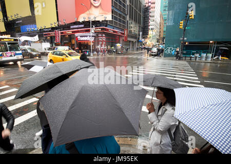 Persone che trasportano gli ombrelli in attesa a crosswalk sotto la pioggia di New York City STATI UNITI D'AMERICA Foto Stock