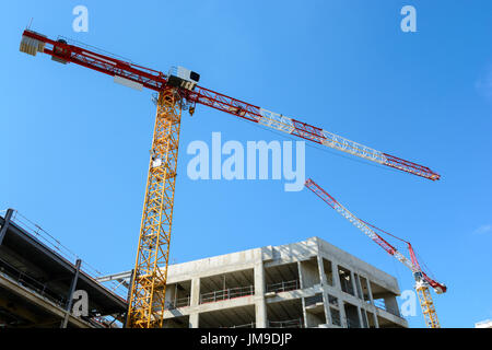 Basso angolo vista di due gru a torre con un edificio in cemento in costruzione con il blu del cielo. Foto Stock