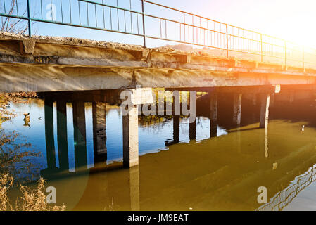 Vista del trascurato il vecchio ponte che consiste di lastre di cemento da qualche parte nel villaggio. Ponte sul fiume con acqua fangosa. Foto Stock