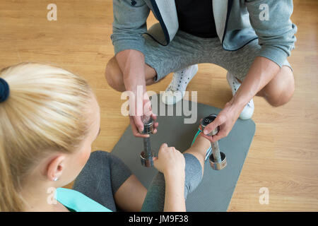 Personal trainer consegna manubri di giovane donna durante la sessione di allenamento Foto Stock