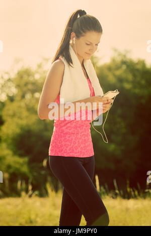 Femmina attraente prendendo una pausa dopo il jogging, tenendo lo smartphone Foto Stock