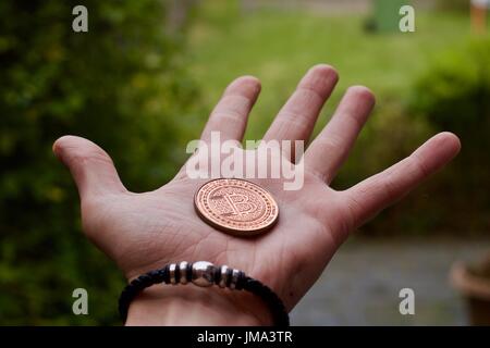 Valuta digitale fisico bitcoin in ottone coin in man mano con bracciale nero. Foto Stock