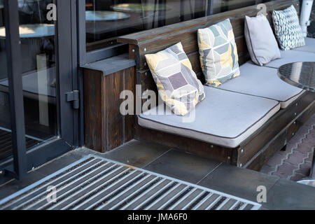 Chiudere fino al di fuori di un ristorante moderno interior posti a sedere in legno con cuscini, tavolo in metallo e parte dello sportello Foto Stock