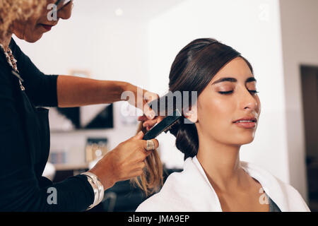 Donna parrucchiere utilizzando una spazzola per capelli per un taglio di capelli al salone. Giovane donna ottenendo un elegante taglio di capelli fatto a salon. Foto Stock