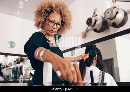 Femmina hair stylist lavorando su una donna 's capelli. Senior donna parrucchiere rendendo un elegante taglio di capelli. Foto Stock