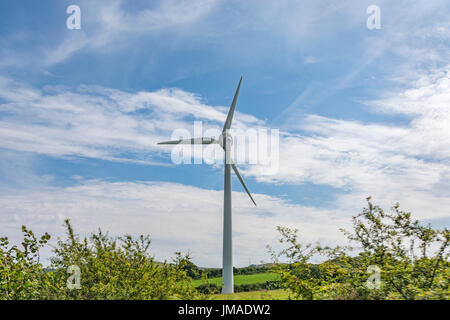 Gigante turbina eolica / generatore eolico in un campo impostato contro il cielo blu e sun. Metafora energia pulita, energie rinnovabili, energia eolica. Foto Stock