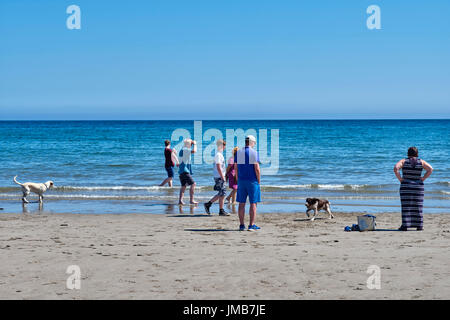 Le persone e i cani a piedi la linea di galleggiamento sulla spiaggia Laxey, Isola di Man Foto Stock