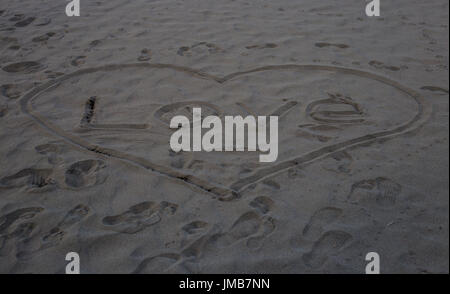 La parola amore Scritta sulla sabbia grigia a forma di cuore sulla spiaggia nelle prime ore del mattino in estate. Foto Stock