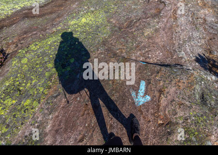 Ombra umana a piedi nella direzione sbagliata, contro la freccia blu sulla roccia Foto Stock