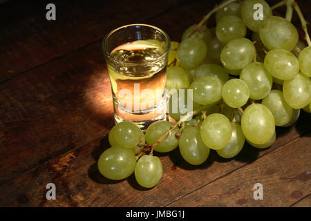 Bicchiere pieno di uva vodka "grappa" vicino a grappolo di uva sulla vecchia superficie in legno Foto Stock