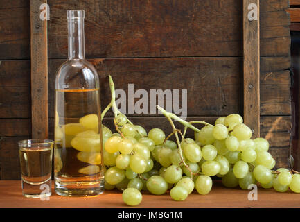 Bicchiere pieno di uva vodka italiana "grappa" vicino a bottiglia e grappolo di uva sul vecchio sfondo di legno Foto Stock