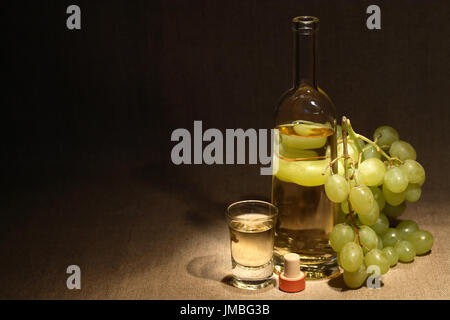 Bicchiere pieno di uva vodka italiana "grappa" vicino a bottiglia e grappolo di uva sul vecchio sfondo canvas Foto Stock