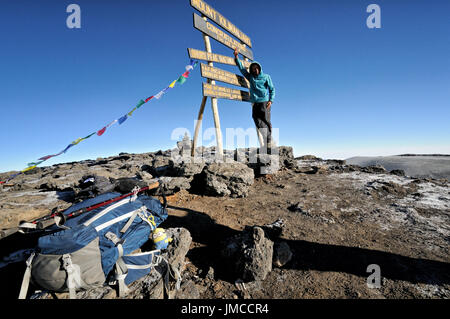 Scalatore africana pone per le foto accanto al cartello marcatura Uhuru Peak, Parco Nazionale del Kilimanjaro, Tanzania Foto Stock