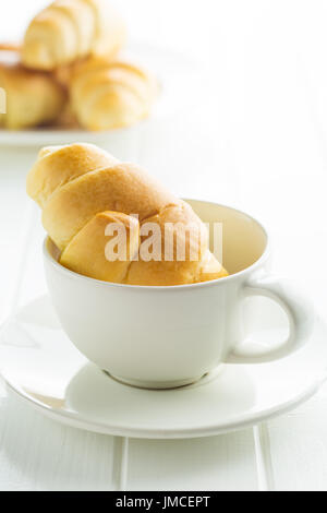 Dolci deliziosi croissant e la tazza di caffè sul tavolo bianco. Foto Stock
