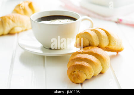 Dolci deliziosi croissant e la tazza di caffè sul tavolo bianco. Foto Stock