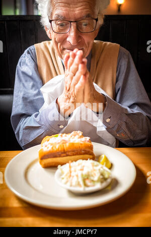 Il vecchio uomo strofina le mani in attesa di mangiare il suo cibo preferito in un ristorante. Lobster roll in costa del Maine. Foto Stock